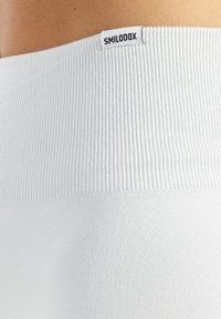 Białe legginsy prążkowane o teksturowanym wykończeniu z czarną nalepką z napisem "SMILODOX" umieszczoną na pasku.