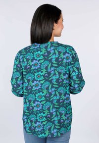 Blumenbluse in Dunkelblaugrün mit blauen und grünen Blumenmustern und roten Akzenten; lockere Passform und Dreiviertelärmel.
