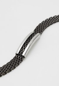 Bracciale intrecciato nero con chiusura magnetica in argento lucido, caratterizzato da una superficie liscia e una forma allungata per una vestibilità sicura.