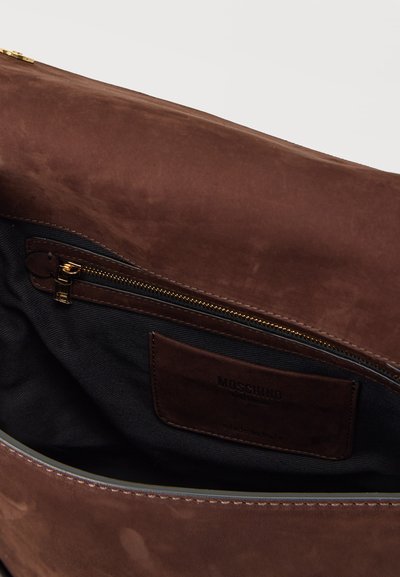Intérieur d'un sac à main en cuir marron montrant une doublure en tissu noir, une poche zippée avec une fermeture éclair dorée, et un patch d'étiquette de la marque Moschino.