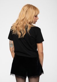 Black cotton t-shirt with short sleeves and a cropped design, paired with black velvet shorts featuring lace trim, seen from the back.