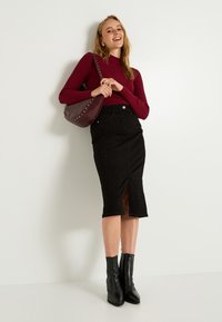 Jupe tube en denim noir avec de petites accents cloutés, dotée d'une fente à l'avant. Associée à un pull côtelé bordeaux et un sac à épaule bourgogne.