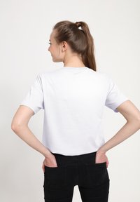 Lichtgrijs, kortärmelig T-shirt met een ronde hals, gemaakt van katoen. Gecombineerd met zwarte, aansluitende jeans; handen in de zakken. Eenvoudig ontwerp.