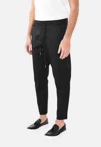 Pantaloni jogger neri, leggeri, con elastico in vita e cordino. Presentano gambe affusolate e tasche laterali. Texture liscia.