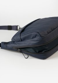 Zaino blu navy in nylon testurizzato con cerniera sul compartimento principale. Presenta un design piatto e una tracolla regolabile.