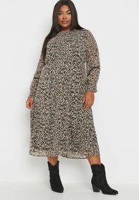 Midi-mekko, jossa on leopardikuvio beige ja mustana, kevyt kangas, pitkät hihat, joustava vyötärö ja levenevä hame. Yhdistetty mustiin nilkkureihin.