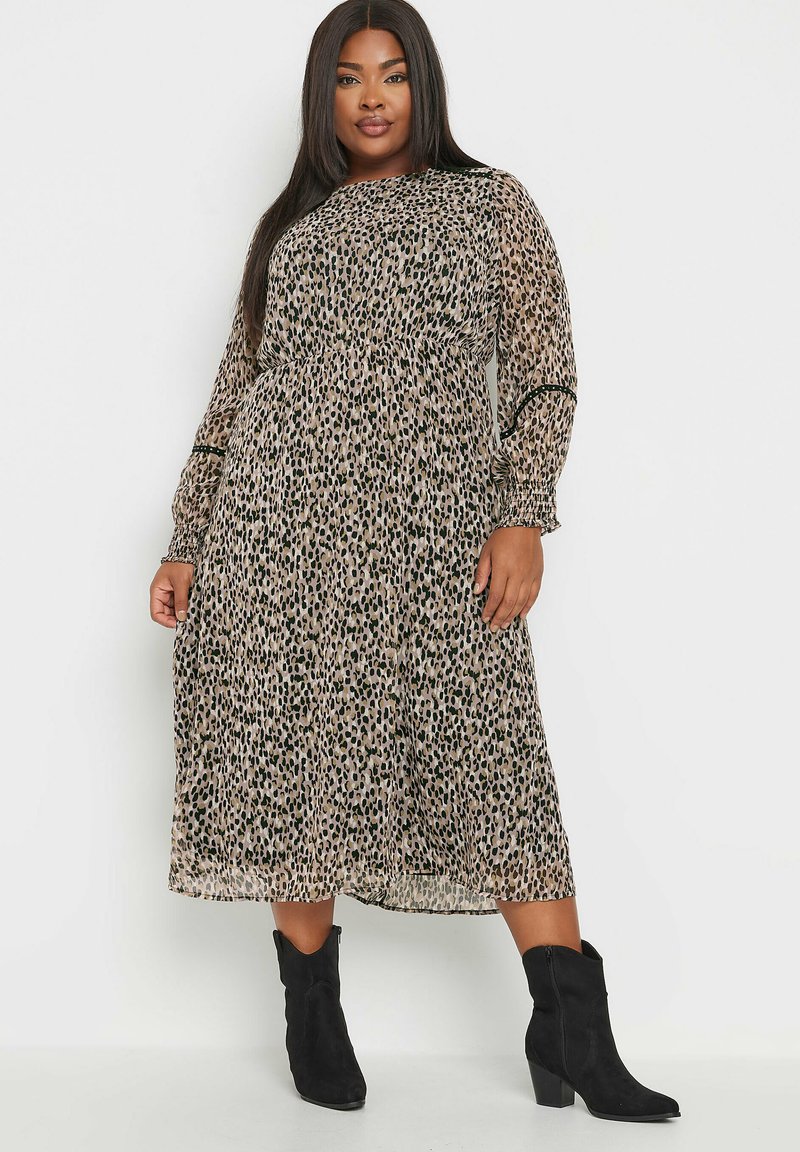 Midi-mekko, jossa on leopardikuvio beige ja mustana, kevyt kangas, pitkät hihat, joustava vyötärö ja levenevä hame. Yhdistetty mustiin nilkkureihin.