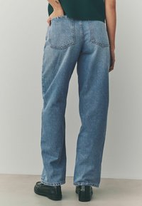 Lichtblauwe, ruime spijkerbroek van denim, met een hoge taille, twee achterzakken en subtiele vervaging. Gecombineerd met zwarte schoenen.