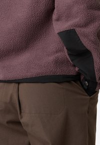 Pullover in pile color malva con dettagli in nylon nero sui polsini. Tessuto textured e morbido, abbinato a pantaloni marroni con dettagli delle tasche discreti.