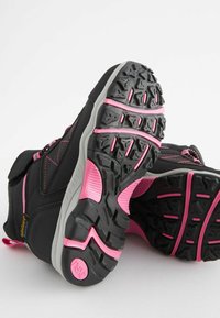 Scarpe da trekking nere e rosa con suola in gomma testurizzata, punta rinforzata e cuciture a contrasto, progettate per aderenza e durabilità.