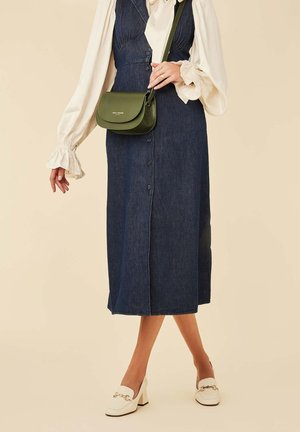 Denim midi-jurk met knopen aan de voorkant en een getailleerde pasvorm, gecombineerd met een groene schoudertas en witte блокhakken loafers. Crème blouse met gerimpelde mouwen.