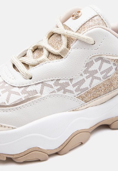Λευκό και μπεζ αθλητικό παπούτσι με λαμπερές χρυσές λεπτομέρειες, πλευρικό πάνελ με μοτίβο, χοντρή σόλα και μπεζ κορδόνια δεμένα σε σταυρωτό σχέδιο.