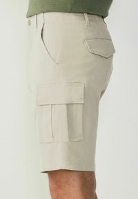 Shorts cargo beige en tissu léger, dotés de poches latérales et arrière, d'une taille plate et d'une coupe décontractée, s'arrêtant juste au-dessus du genou.