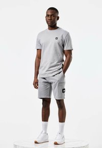 Grå bomulls t-skjorte og shorts sett, med et lite logo-patch, sidelomme på shortsen, sammen med hvite sneakers og hvite sokker til knærne.
