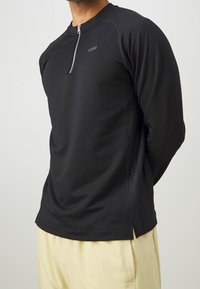 Schwarzes, langärmeliges Sportshirt mit halbem Reißverschluss und strukturierten Einsätzen an den Seiten. Verfügt über einen Rundhalsausschnitt und ein schlank geschnittenes Design.