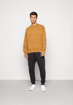 Sennepsmønstrede sweatshirts med ribbede manchetter, parret med sorte sweatpants med satinstriber i siderne og hvide sneakers.