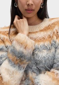 Strukturierter Pullover in den Farbtönen Beige, Braun und Grau mit einem flauschigen, wellenförmigen Design. Verfügt über einen gerippten Ausschnitt und eine lockere Passform.