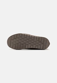 Suela de zapato hecha de goma, que presenta una superficie texturizada con un patrón hexagonal y diversas ranuras de tracción, en un color marrón claro.
