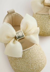 Goldene Glitzer-Ballettschuhe mit einer weichen elfenbeinfarbenen Schleife und einem metallischen Akzent. Das Design verfügt über eine abgerundete Zehenpartie und eine strukturierte Oberfläche.