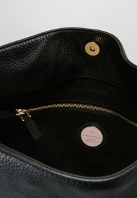 Mustan nahka käsilaukun sisustus, jossa on vetoketjullinen tasku ja kultaiset yksityiskohdat. Mukana pyöreä brändilappu ja teksturoitu vuori.