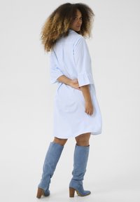 Abito camicia a righe blu e bianche con maniche a tre quarti, polsini arricciati e vestibilità ampia, abbinato a stivali di camoscio blu al ginocchio.