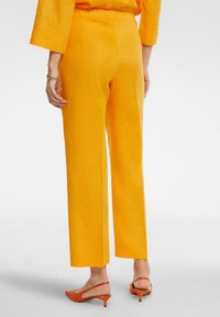 Pantaloni in lino arancioni brillanti con una vestibilità morbida, gamba dritta e una texture liscia; abbinati a tacchi slingback arancioni.