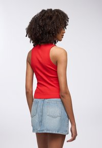 Top a fascia rossa a coste abbinato a una mini gonna di denim blu chiaro. Il tessuto ha una consistenza liscia, mentre la gonna presenta tasche posteriori.