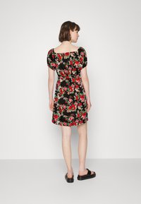 Vestido preto florido com padrões vermelhos e verdes, mangas curtas bufantes, cintura ajustada e comprimento até ao joelho. Usado com sandálias planas pretas.