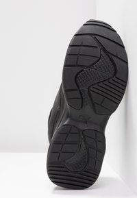 Sneaker nera con suola in gomma testurizzata, caratterizzata da un motivo battistrada, forma sagomata e un logo in rilievo discreto sul tallone.