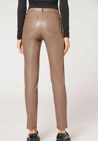 Pantaloni in finta pelle marrone con una vestibilità slim, vita piatta e due tasche posteriori. Texture liscia con una finitura lucida.
