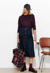 Jupe en denim avec des boutons sur le devant, associée à un pull violet foncé et un tote bag à carreaux, complétée par des chaussettes bordeaux et des chaussures noires.