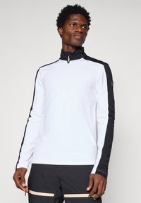 Valge pika varrukaga topp mustade külgpaneelite, kõrge krae ja poolikuga tõmblukk. Valmistatud kergest, venitavast kangast.