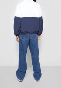 Navy and white color-blocked jacket with a relaxed fit, paired with loose blue denim jeans. Material appears lightweight with elastic cuffs.