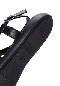 Black leather sandal featuring thin adjustable straps, a textured rubber sole, and a flat profile for casual wear.