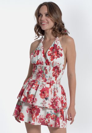 Robe halter fleurie blanche avec de vives motifs de fleurs rouges et vertes. Comprend une taille smockée, des volants à plusieurs niveaux et un corsage ajusté.
