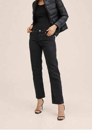 Mujer con chaqueta acolchada corta negra, top negro sin mangas, jeans negros de talle alto y pierna recta, y sandalias negras de tiras con tacón alto.