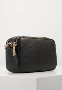 Borsa nera in pelle con superficie testurizzata, zip dorata e forma rettangolare. Presenta un attacco per portachiavi e un design minimalista.