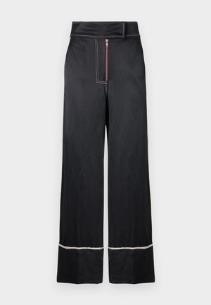 Pantalones de pierna ancha negros con una cintura alta, que cuentan con un cierre frontal de cremallera y costuras blancas en contraste a lo largo del dobladillo y los laterales.