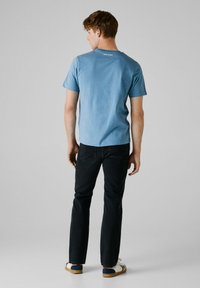 Lysblå bomulds t-shirt med rund hals og korte ærmer, set fra ryggen. Sammen med mørke jeans og casual slip-on sko.