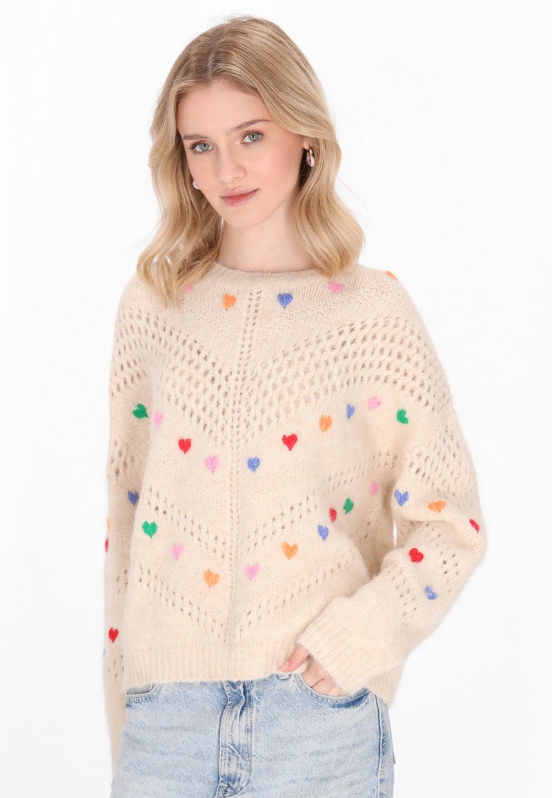 Maglione beige lavorato a maglia con motivo aperto e motivi a cuore multicolori. Vestibilità ampia con polsini e orlo a coste.