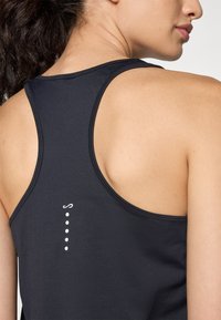 Must mustriga tank top, millel on racerback disain, valge logo ja viis punkti keskosas. Sile tekstuur ja kehakujuline vorm.