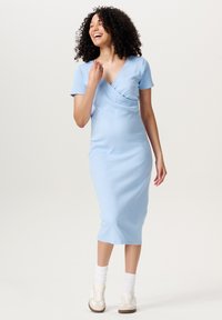 Light blue, fitted dress with short sleeves and a wrap design. Worn with white ankle socks and beige sneakers. Smooth fabric texture.