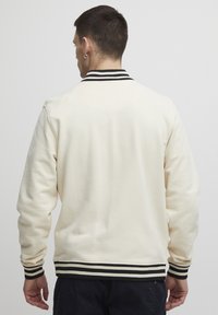 Cream-colored sweatshirt with a ribbed black and white striped collar and cuffs, featuring a smooth texture and relaxed fit.