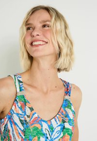 Top de tirantes multicolor con un patrón floral, escote redondeado y herrajes decorativos plateados en los tirantes. Fabricado con un tejido ligero.