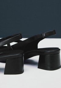 Sandalias de tacón bloque negro en piel suave con punta redondeada y tiras delgadas. Destacan por su diseño de tacón geométrico y estilo minimalista.