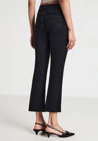 Jeans svasati in denim nero con vita alta, orlo grezzo e tasche posteriori discrete, abbinati a scarpe con tacco nere a slingback.