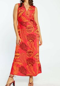 Robe maxi rouge avec un design portefeuille, présentant des motifs de feuilles jaunes et brunes. Sans manches avec un cordon ajustable à la taille, tissu fluide.