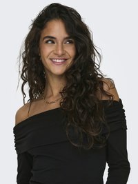 Mladá žena s dlhými kučeravými vlasmi sa usmieva, má na sebe čierny top so spadnutými ramenami a zlatý reťazový náhrdelník, pozerá sa do strany.