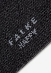 Detailný záber na čiernu pletenú tkaninu s nápisom "FALK E HAPPY" tkaným svetlosivou priadzou diagonálne.