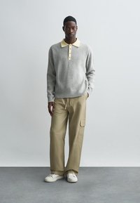 Grå ribbad tröja med en gul krage, knappslå; kombinerad med beige cargobyxor och vita sneakers mot en neutral bakgrund.